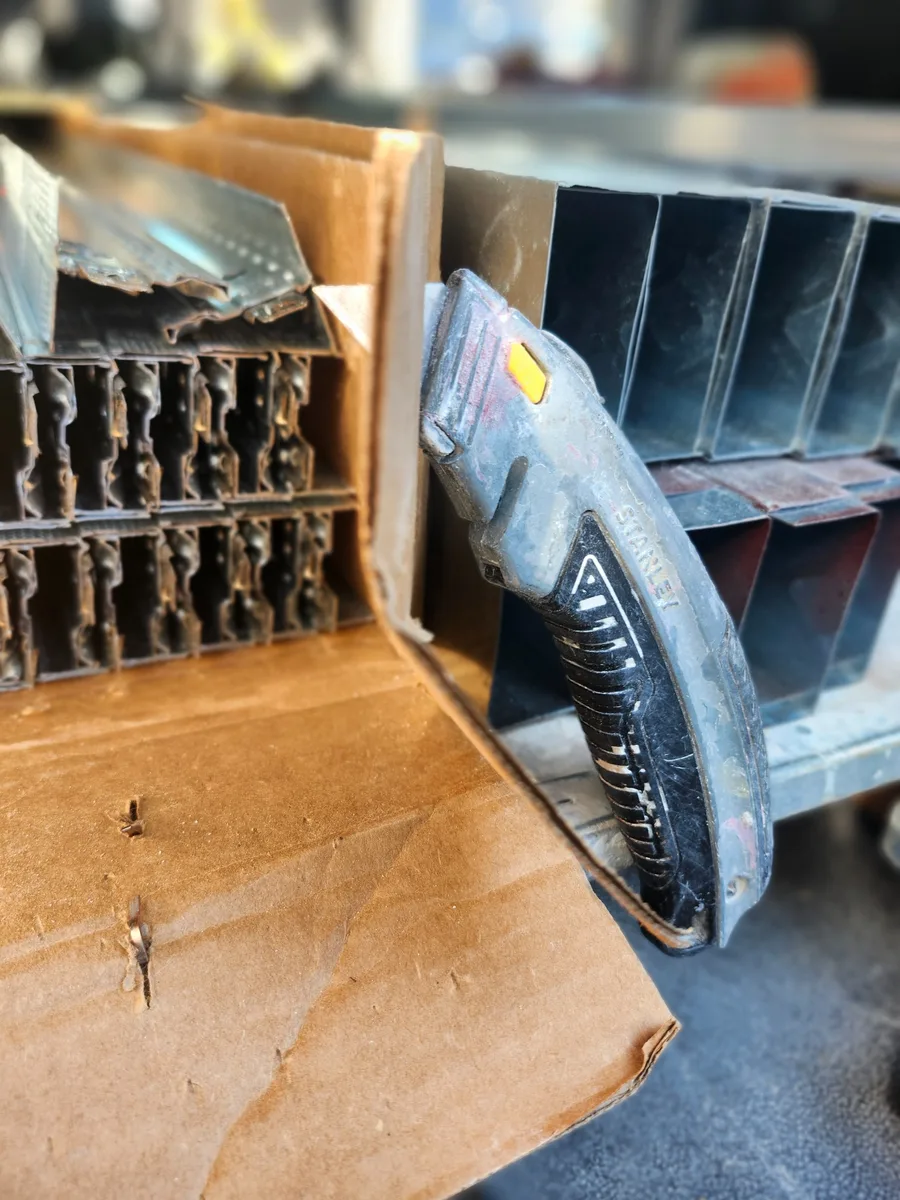 A field-used curved quick-change retractable utility knife stored beside metal framing material.